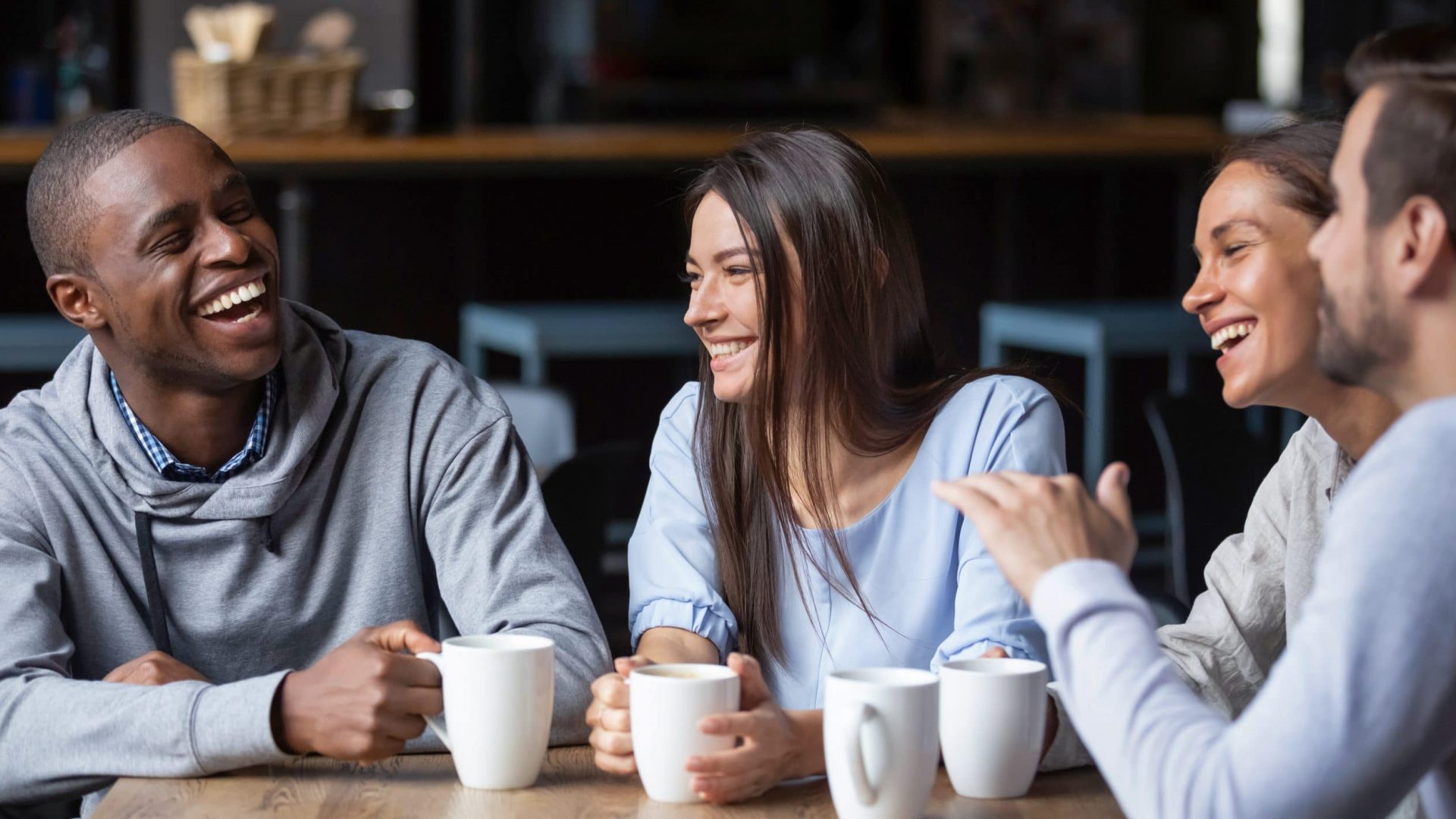 Multiracial friends girls and guys having fun laughing drinking coffee tea in coffeehouse, happy diverse young people talking joking sitting together at cafe table, multicultural friendship concept